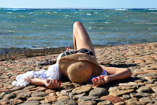 caucasian woman in straw hat lying on the stone beach in Egypt