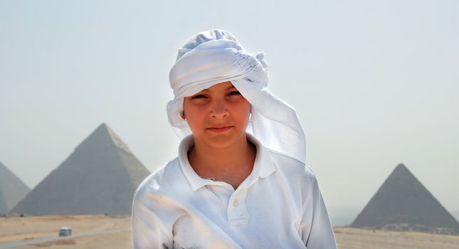 teenage caucasian boy tourist in white kerchief over pyramids on Giza in Egypt