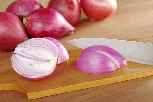 Cutting red onions on wooden cutting board (Selective Focus, Focus on the cut onion and the knife)