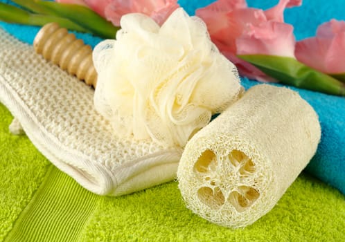 Green and blue bath towels with a bath spa kit and a pink gladiolus (Selective Focus, Focus on the the front of the round sponge)