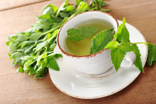 Tea made of fresh mint leaves on wood (Selective Focus, Focus on the front of the cup and the top of the mint leaves on the handle) 