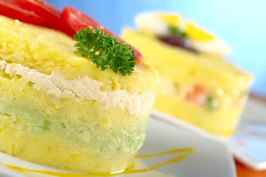 Peruvian dish called Causa, which is made of mashed yellow potatoes, and here, filled with avocado and chicken (Selective Focus, Focus on the parsley and the front of the meal) 