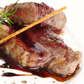 Meat with red pepper sauce, rosemary and a salt stick as garnish (Selective Focus, Focus on the front)