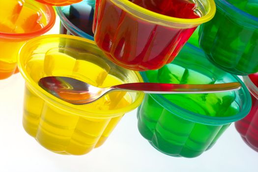 Colorful jellies in plastic bowls arranged in a pile with a teaspoon (Selective Focus, Focus on the teaspoon) 