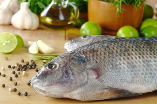 Raw fish called Tilapia surrounded by spices, herbs and seasonings (Selective Focus, Focus on the head and the belly part of the fish)