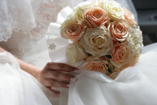 The bouquet from roses lays on a dress of the bride
