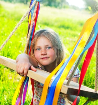 Young cute girl on swing with ribbons in the garden