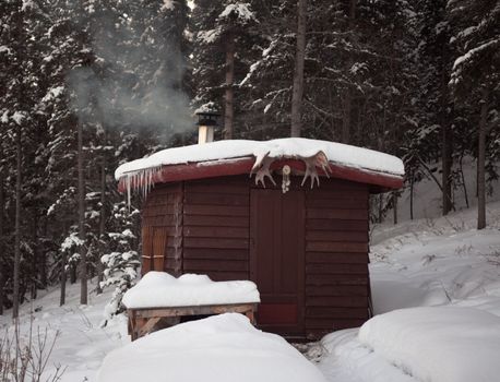 Smoking wood stove is heating up small sauna hut in winterly boreal forest