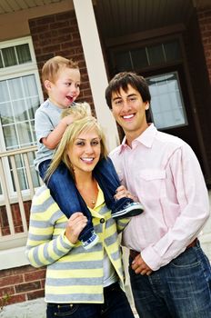 Young happy family standing in front of new home