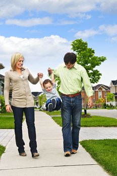 Young happy family playing with son on sidewalk