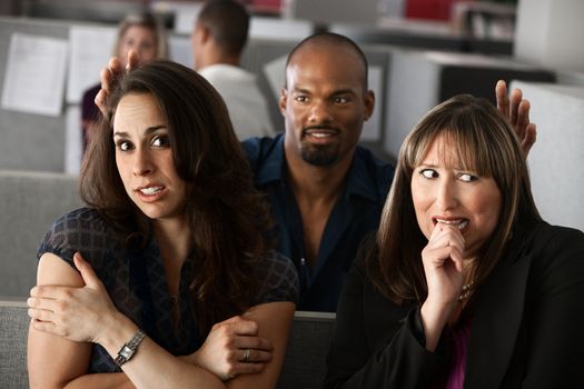 Man standing behind two scared women in office cubicle