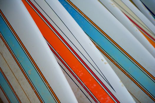 A row of sandy, striped beach surfboards with bright colors