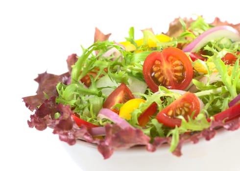 Fresh mixed salad from red-leaf lettuce, curly endive (frisee), cherry tomato, red onion, cucumber and red and yellow bell pepper in white bowl on white (Selective Focus, Focus on the cherry tomato half) 