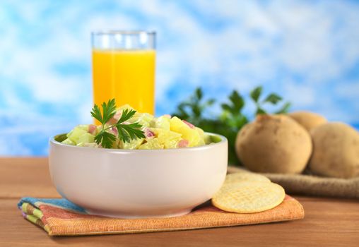 Potato salad made of cooked potatoes, red onions and cucumber, seasoned with a mayonnaise dressing and garnished with a parsley leaf with crackers on the side and orange juice in the back (Selective Focus, Focus on the front of the salad and the leaf)