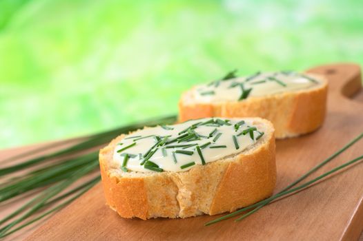 Baguette slices with soft cheese and chives on cutting board (Selective Focus, Focus on the front of the first baguette)