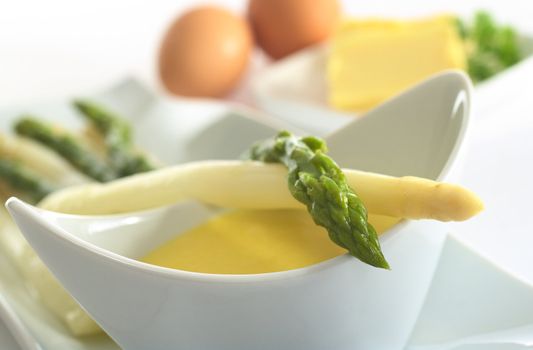 Asparagus lying on a bowl full of Hollandaise sauce (Very Shallow Depth of Field, Focus on the head of the green asparagus)