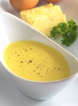 Hollandaise sauce with black pepper on top and its ingredients, egg and butter in the back (Selective Focus, Focus in the middle of the bowl)