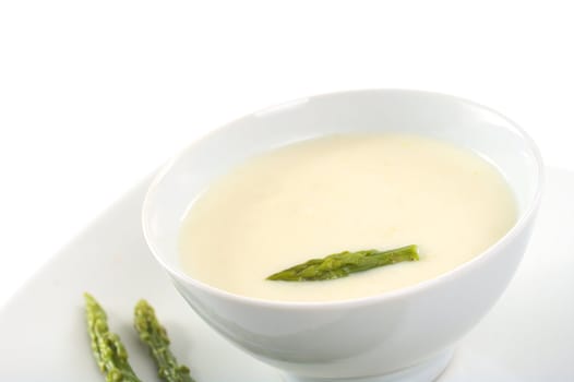 Cream of asparagus with a green asparagus head on top in a white bowl (Very Shallow Depth of Field, Focus on the asparagus head in the soup)