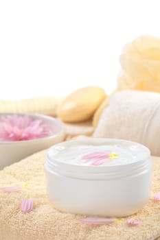 Soft body, hand and face cream with pink petals on top in a bathroom/spa setting (Selective Focus, Focus on the horizontal/back petal on the cream)