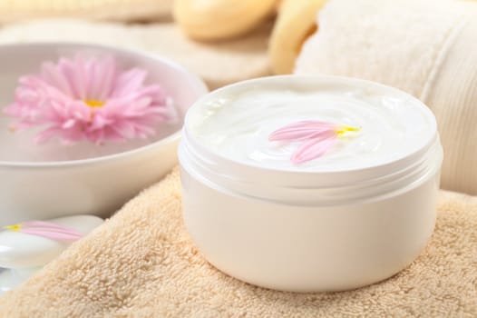 Soft body, hand and face cream with pink petals on top in a bathroom/spa setting (Selective Focus, Focus on the horizontal/back petal on the cream)