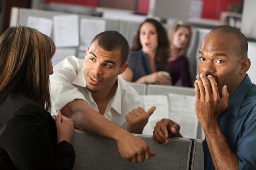 Embarrassed man with hand over mouth standing with coworkers