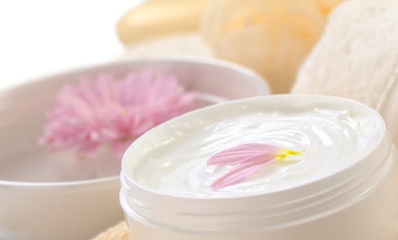 Soft body, hand and face cream with pink petals on top in a bathroom/spa setting (Selective Focus, Focus on the horizontal/back petal on the cream)