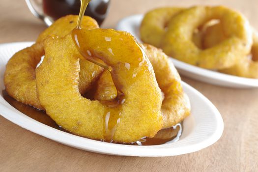 Pouring Chancaca syrup (kind of honey) on the popular Peruvian dessert called Picarones made from squash and sweet potato, served on plastic plate (Selective Focus, Focus on the front)