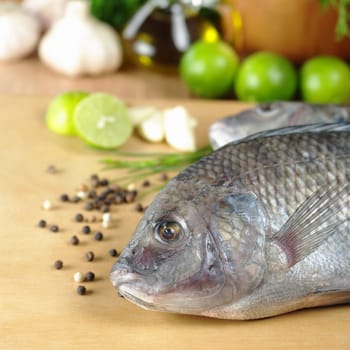 Raw fish called Tilapia surrounded by spices, herbs and seasonings (Selective Focus, Focus on the head and the eye of the fish)