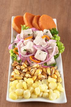 Peruvian-style ceviche made out of raw dogfish (Spanish: tollo), red onions and aji (Peruvian hot pepper) and served with corn, roasted corn (cancha) and cooked sweet potato (Selective Focus, Focus on the front of the fish)