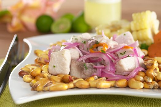 Peruvian-style ceviche made out of raw mahi-mahi fish (Spanish: perico), red onions and aji (Peruvian hot pepper) and served with roasted corn (cancha) and cooked corn. In the back Peruvian cocktail called "Pisco Sour", limes and a flower. (Selective Focus, Focus on the front of the fish)