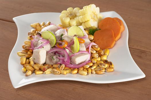 Peruvian-style ceviche made out of raw mahi-mahi fish (Spanish: perico), red onions, limes and aji (Peruvian hot pepper) and served with roasted corn (cancha) and cooked corn cob as well as cooked sweet potato (Selective Focus, Focus on the front of the fish)