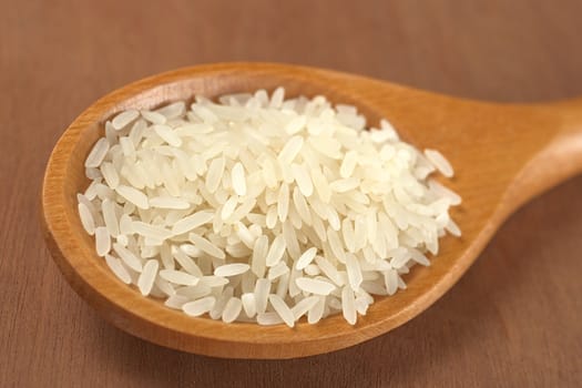 Raw rice grains on a wooden spoon (Selective Focus, Focus on the middle and the front of the grains)