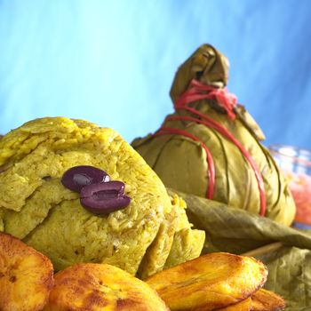 Traditional Peruvian food called Juane from the jungle area, in which rice, eggs and different kind of meat is wrapped into bijao leaves, and is served with fried plantains and black olives (Selective Focus, Focus on the olives and the front of the rice)