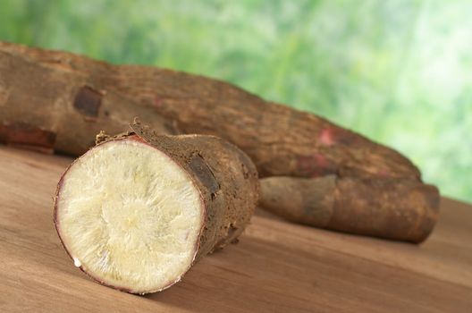 Raw cassava (lat. Manihot esculenta) on wood with green background (Selective Focus, Focus on the front)