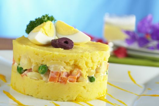 Traditional Peruvian dish called Causa made of mashed yellow and white potato mixed with aji (hot pepper) and lime juice and filled with vegetables (corn, peas, carrots) and mayonnaise and garnished with eggs and olives (Selective Focus, Focus on the front) 