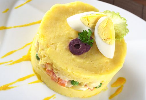 Traditional Peruvian dish called Causa made of mashed yellow and white potato mixed with aji (hot pepper) and lime juice and filled with vegetables (corn, peas, carrots) and mayonnaise and garnished with eggs and olives (Selective Focus, Focus on the olives and the top) 