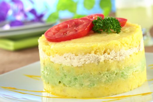 Peruvian dish called Causa made out of mashed potato mixed with lime juice and aji (hot pepper) and filled with avocado and chicken and garnished with tomato slices and parsley (Selective Focus, Focus on the front)