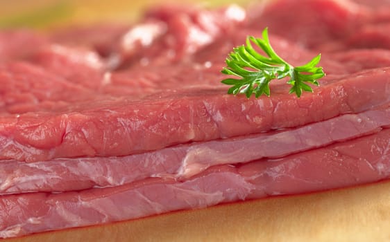 Slices of fresh beef meat garnished with parsley (Selective Focus, Focus on the front of the meat and the parsley)