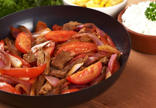 Preparing the Peruvian dish called Lomo Saltado in frying pan (beef, tomato and onions). It is served with French fries and rice. (Selective Focus, Focus on the middle of the pan)