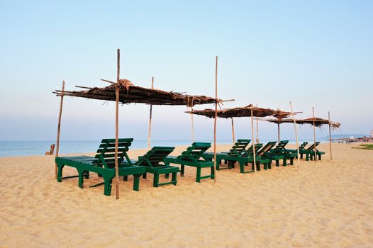 Exotic lean-to of palm leaves and green deck-chairs on tropical beach
