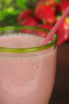 Strawberry milkshake with drinking straw and strawberries in the background (Selective Focus, Focus on front rim of the glass) 