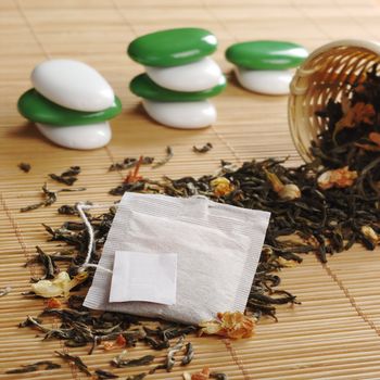 Teabag with empty white label on lose green tea with dried jasmine blossoms and a wooden tea strainer and some white and green stones in the background (Selective Focus, Focus on the teabag and the label)