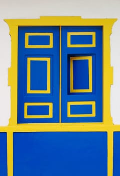 Blue wooden window with yellow frame and a slightly open window in Colombia