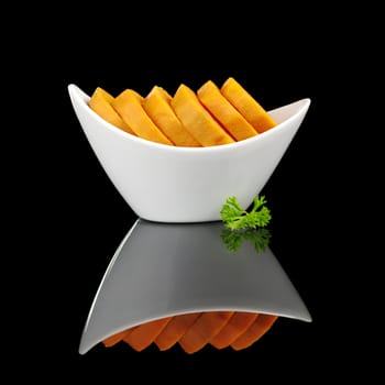 Cooked sweet potato slices (lat. Ipomoea batatas) in white bowl garnished with a parsley leaf and photographed on black  (Selective Focus, Focus on the front) 