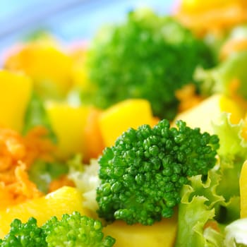 Broccoli on fresh salad (broccoli, mango, carrot, lettuce) in a bowl with blue background (Very Shallow Depth of Field, Focus on the front of the broccoli)