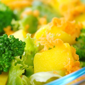 Mango on fresh salad (broccoli, mango, carrot, lettuce) in a glass bowl (Very Shallow Depth of Field, Focus on the front of the mango)