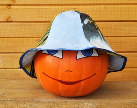 Pumpkin with female face in a colour children's hat, against wooden boards, photo by a Halloween