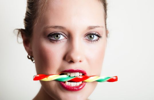 Portait of young woman holding colorful candy in her teeth