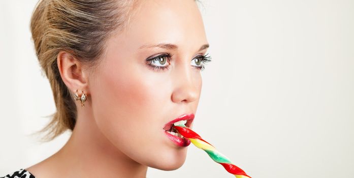 Portrait of a pretty young woman biting colorful lollipop
