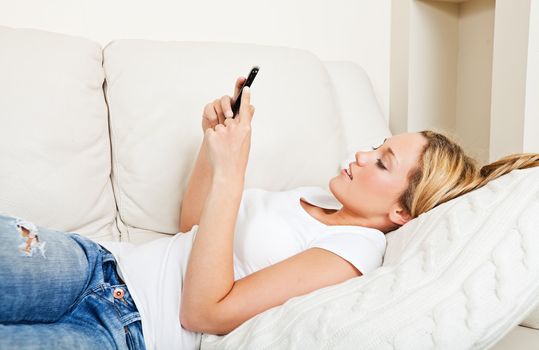 Pretty young woman lying on the couch and texting with her smartphone